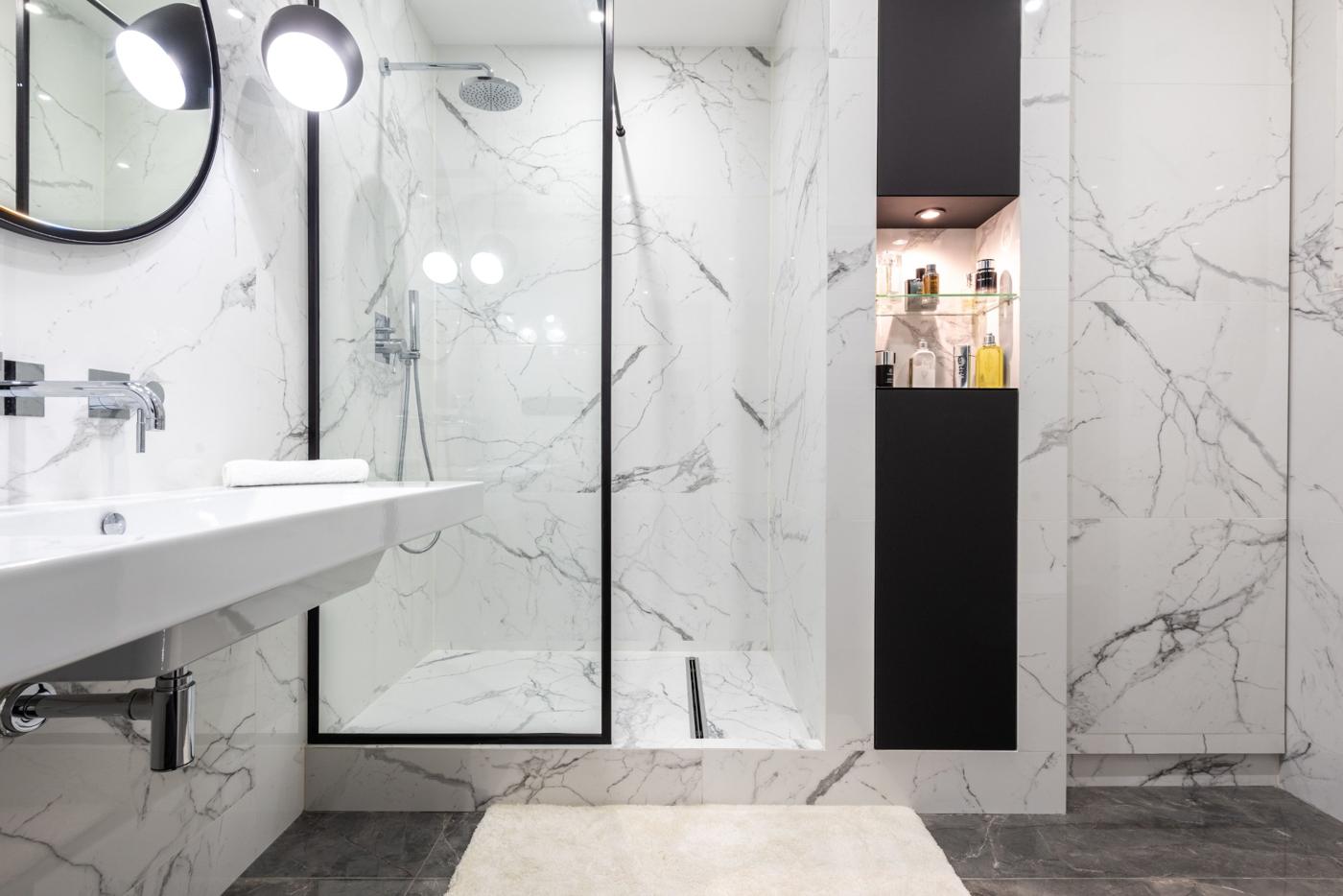 Walk-in shower with marble-look wall panels and black glass frame